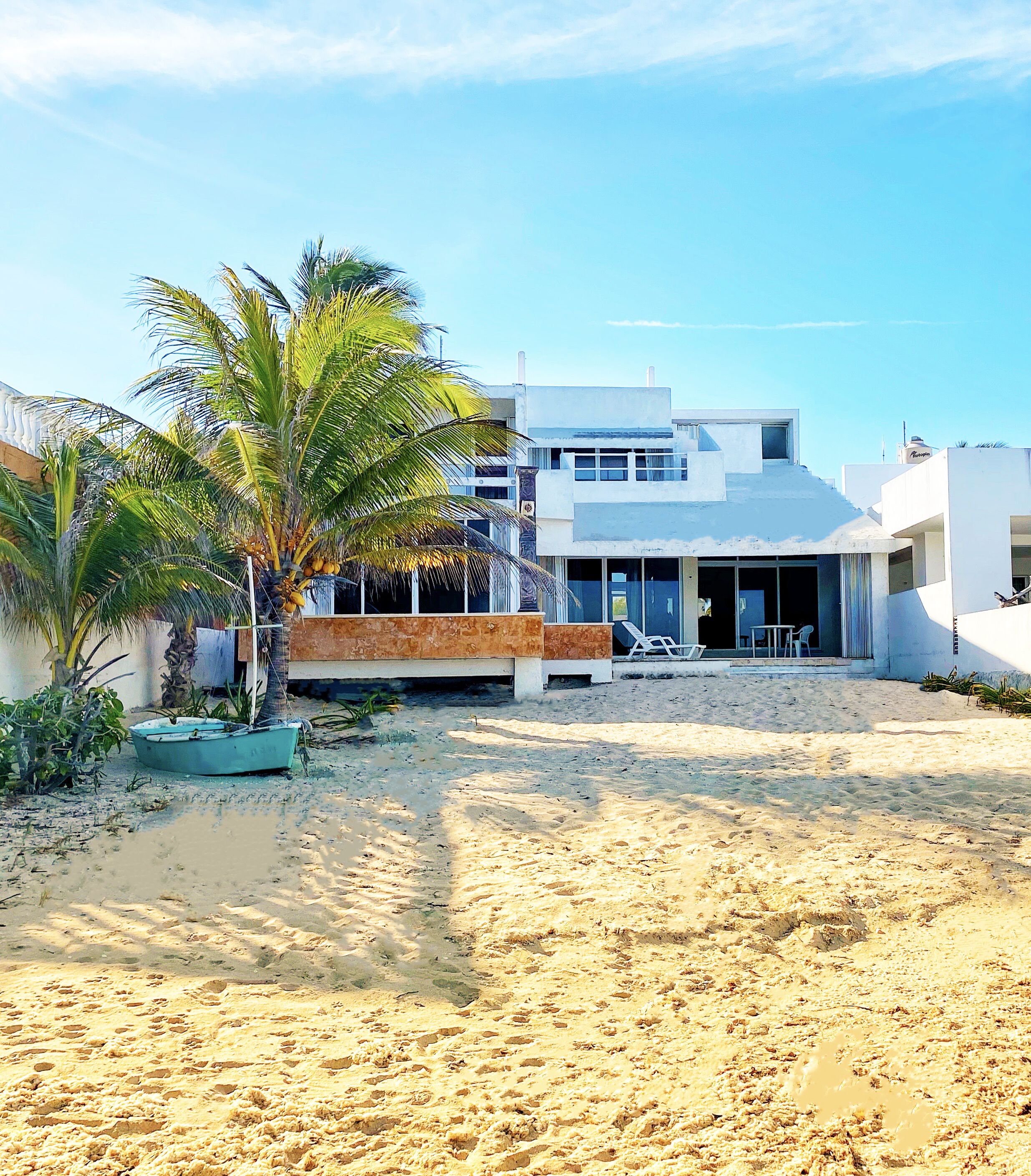 A beachfront property with a modern white building, a palm tree, and a boat on the sand.