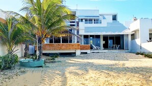 Une propriété située en bord de mer, avec un bâtiment moderne de couleur blanche, un palmier et un bateau sur le sable.