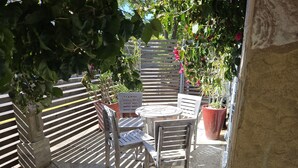 Eine Terrasse mit rundem Tisch und zwei Stühlen, umgeben von Kübelpflanzen und einem Holzzaun.