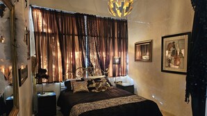 Ein Schlafzimmer mit einem großen Bett, einer dekorativen Deckenleuchte, Vorhängen und gerahmten Kunstwerken an den Wänden.