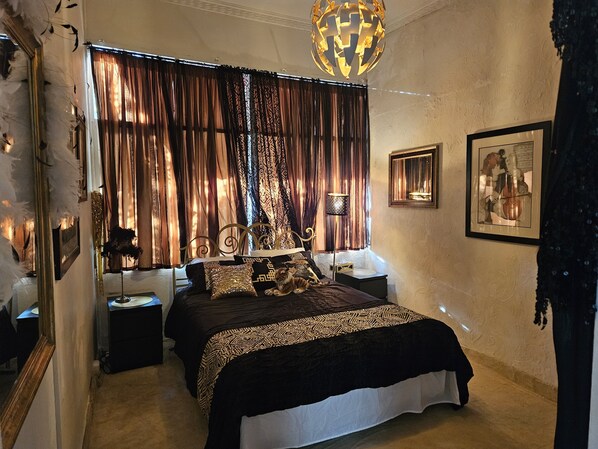 A bedroom with a large bed, a decorative ceiling light, curtains, and framed artwork on the walls.