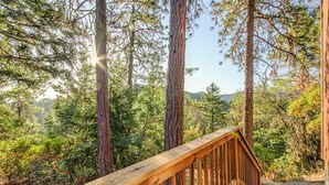 Una terraza de madera con vistas a altos pinos y una cadena montañosa distante.