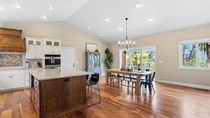 Una cocina amplia con una isla grande, armarios de madera y un comedor con candelabro.