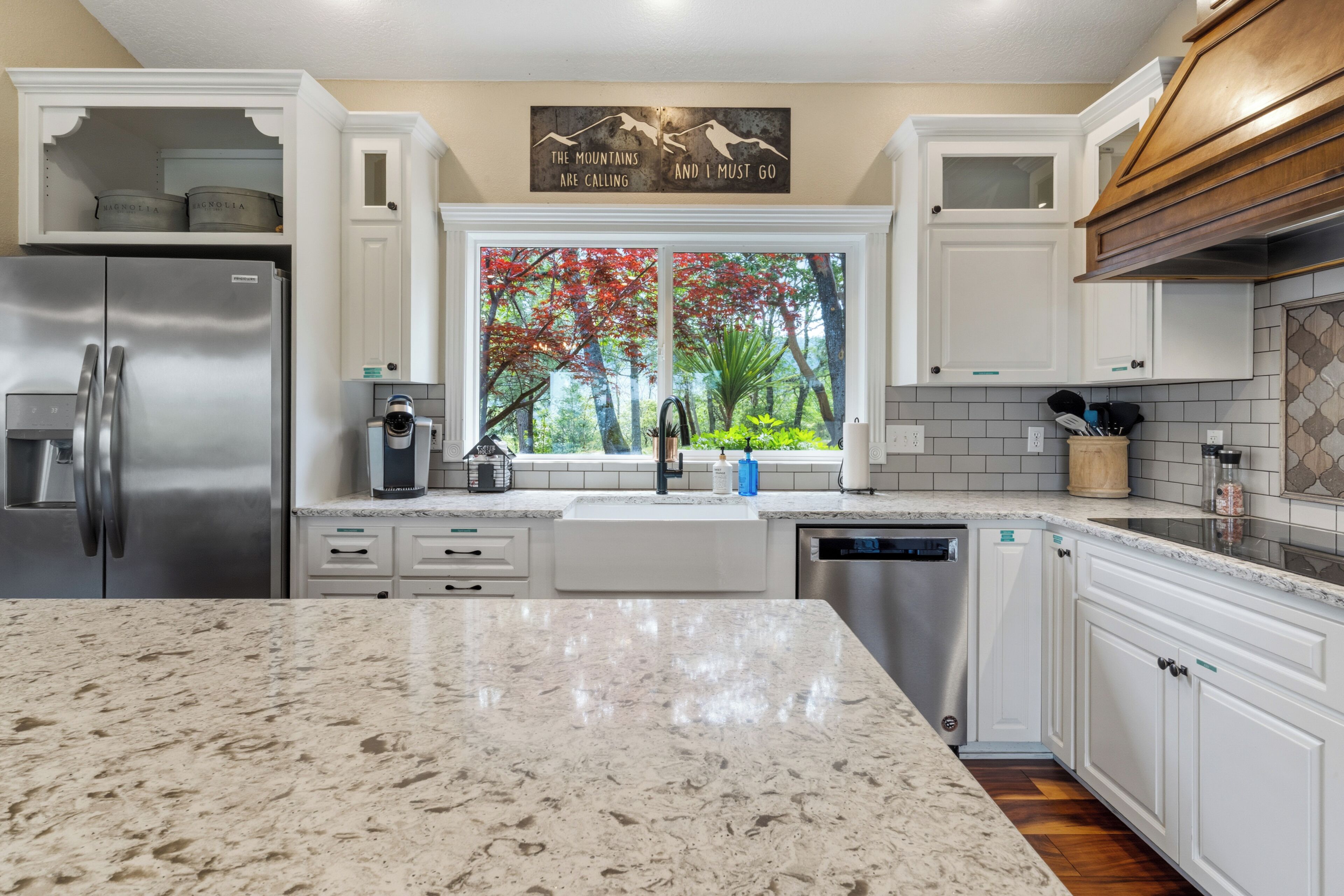 A modern kitchen with white cabinetry, stainless steel appliances, and a large window with a view of trees.