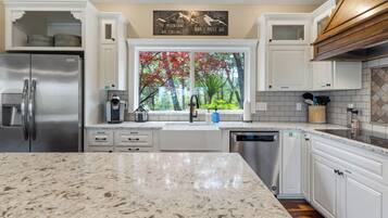 A modern kitchen with white cabinetry, stainless steel appliances, and a large window with a view of trees.