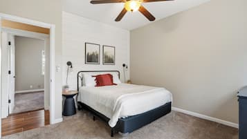 A bedroom with a bed, a ceiling fan, a nightstand, a wall-mounted lamp, and two framed pictures.