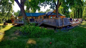 A wooden cabin with a deck, surrounded by lush greenery and trees. - HISTORIC RUSHING WATER LODGE on the rogue river was built in 1910 (Eagle Point)