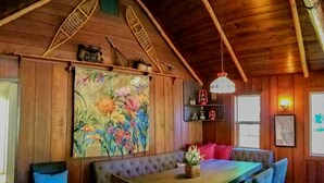 A wooden interior with a dining table, chairs, a bench, a hanging light fixture, and a large floral painting. - HISTORIC RUSHING WATER LODGE on the rogue river was built in 1910 (Eagle Point)