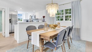 Een moderne keuken met witte kastjes, een roestvrijstalen koelkast en een eethoek met een houten tafel en stoelen met een patroon.