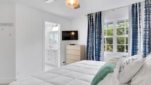 Een slaapkamer met een bed, een televisie, een dressoir en een raam met gordijnen.