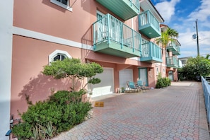 A multi-story building with balconies, a paved driveway, and a small patio area with outdoor furniture.
