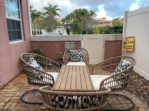An outdoor patio with a wooden table and wicker chairs, surrounded by a pink wall and a white fence. - Beautiful  Townhouse, a few steps from the Beach (Lauderdale-By-The-Sea)