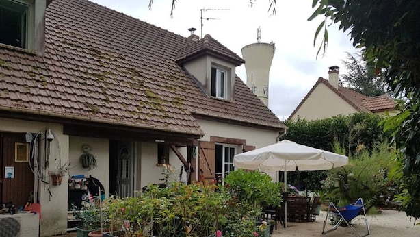 Ein Haus mit einem Ziegeldach, ein Garten mit Topfpflanzen und einem weißen Sonnenschirm.