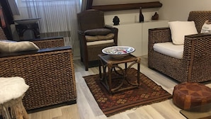 Ein gemütliches Wohnzimmer mit Korbmöbeln, einem kleinen runden Tisch und einem gemusterten Teppich.