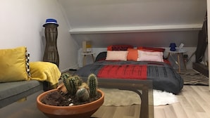 Ein gemütliches Schlafzimmer im Loft-Stil mit Bett, einer Couch, einem Topf mit Kakteen und Lichterketten.