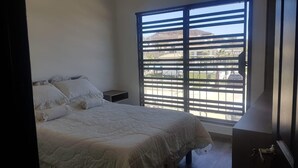 Een slaapkamer met een bed, nachtkastje en een raam met jaloezieën.