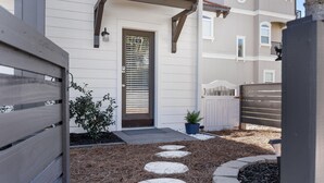 A residential building with a front door, a small garden with stepping stones, and a wooden fence. - Updated Blue Mountain Beach Condo! (Santa Rosa Beach)