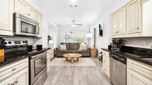 A compact kitchen with modern appliances, a dining area with a sofa, and a ceiling fan. - Updated Blue Mountain Beach Condo! (Santa Rosa Beach)