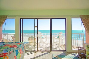 A room with a large sliding glass door leading to a balcony with beach views.