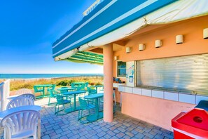A terrace with outdoor seating, a view of the ocean, and a building with a closed shutter.