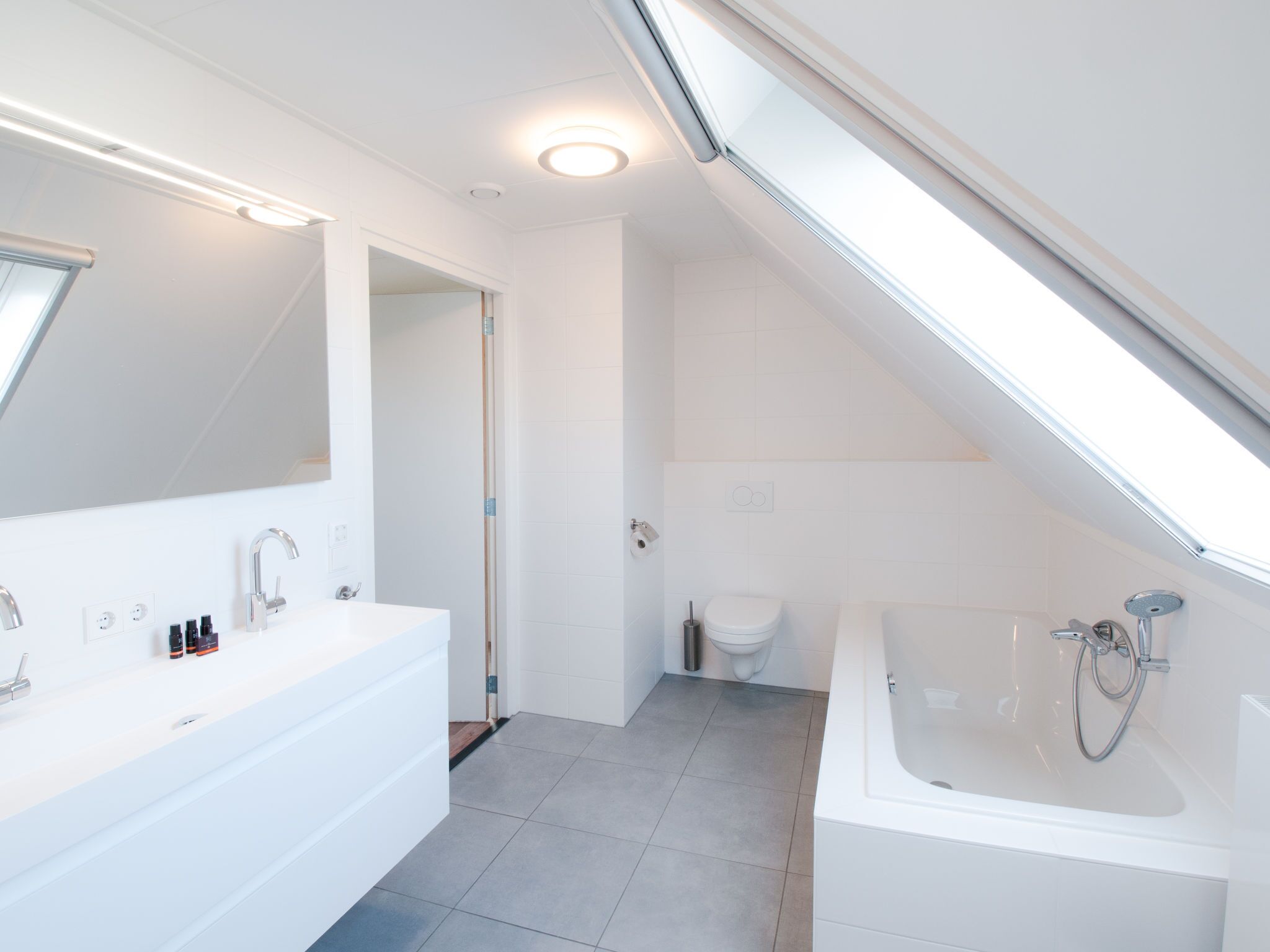 Une salle de bain moderne avec une grande baignoire blanche, un espace douche séparé et un meuble-lavabo doté d’un miroir et de deux vasques.