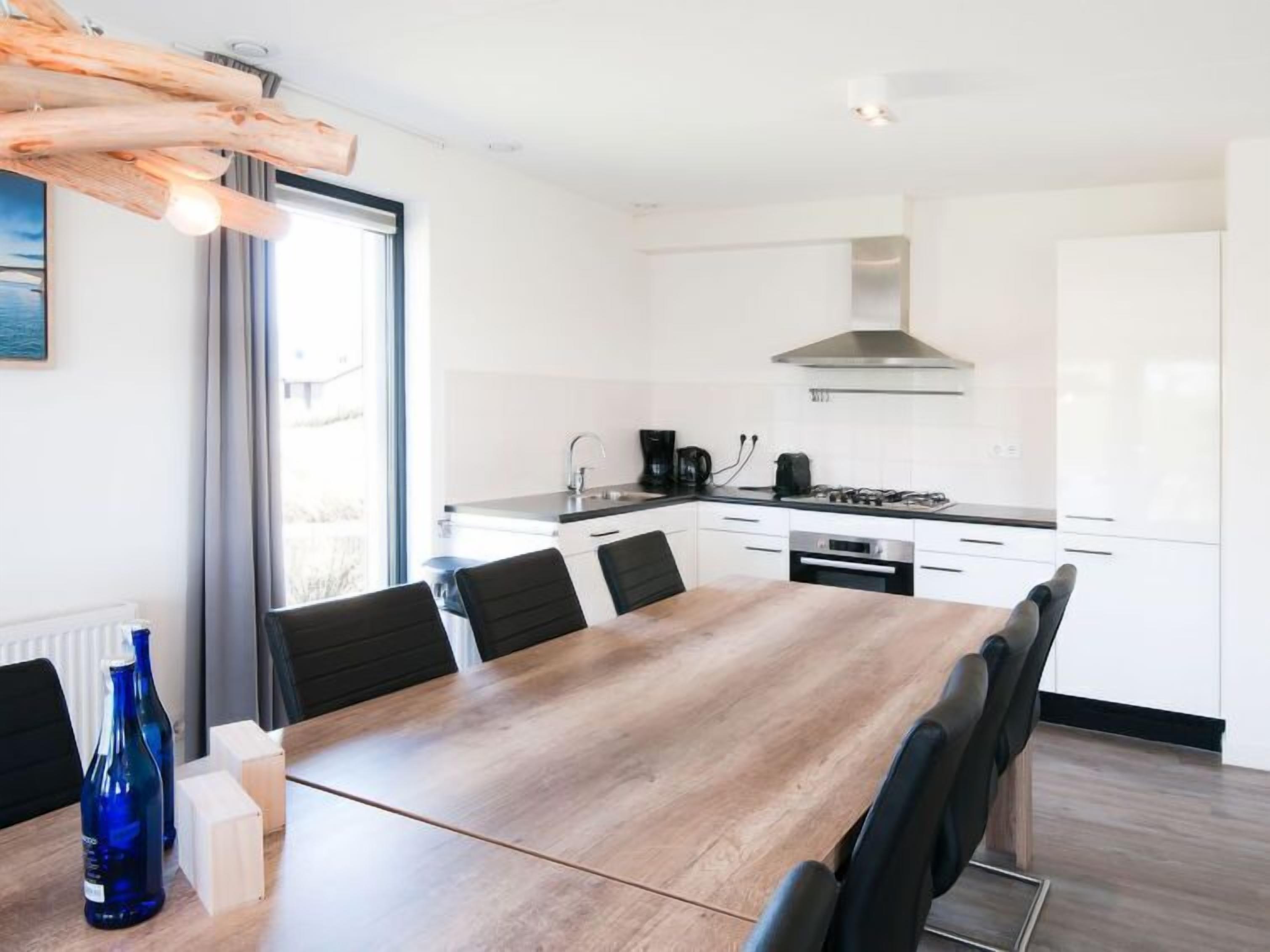 Une cuisine moderne avec des meubles blancs, une table à manger en bois et des chaises noires.