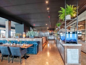 Enjoy a meal in our inviting dining area with a central bench and long table, surrounded by exposed beams and lush greenery.