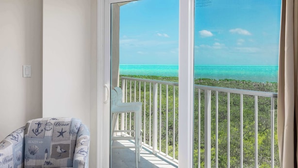 A balcony with a view of the ocean and a chair with nautical-themed fabric.