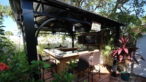 An outdoor patio area with a wooden bar, wicker chairs, and potted plants.