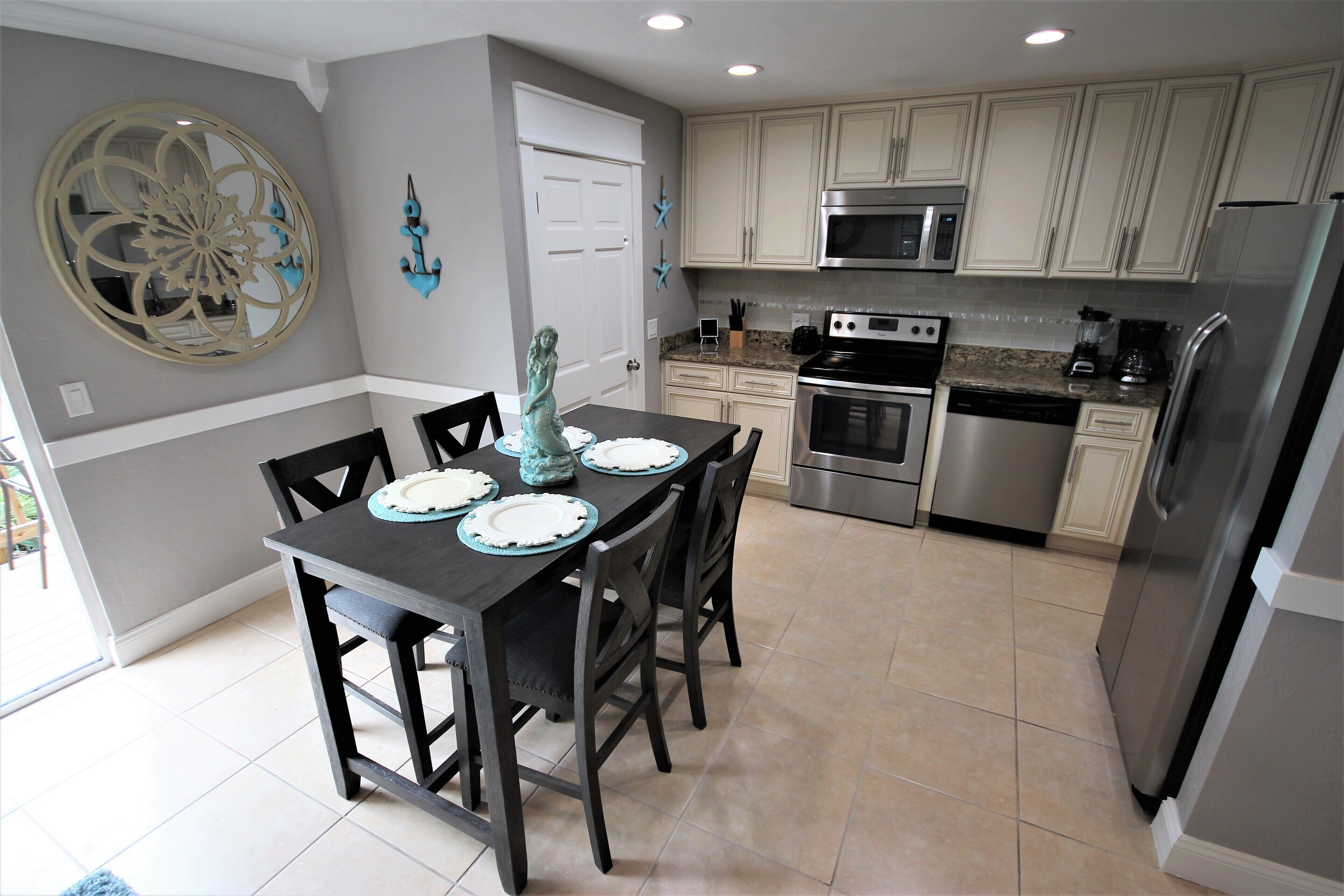 A modern kitchen with white cabinets, stainless steel appliances, and a dining area with a dark table and chairs.