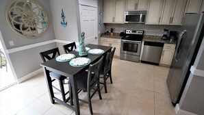 A modern kitchen with white cabinets, stainless steel appliances, and a dining area with a dark table and chairs.