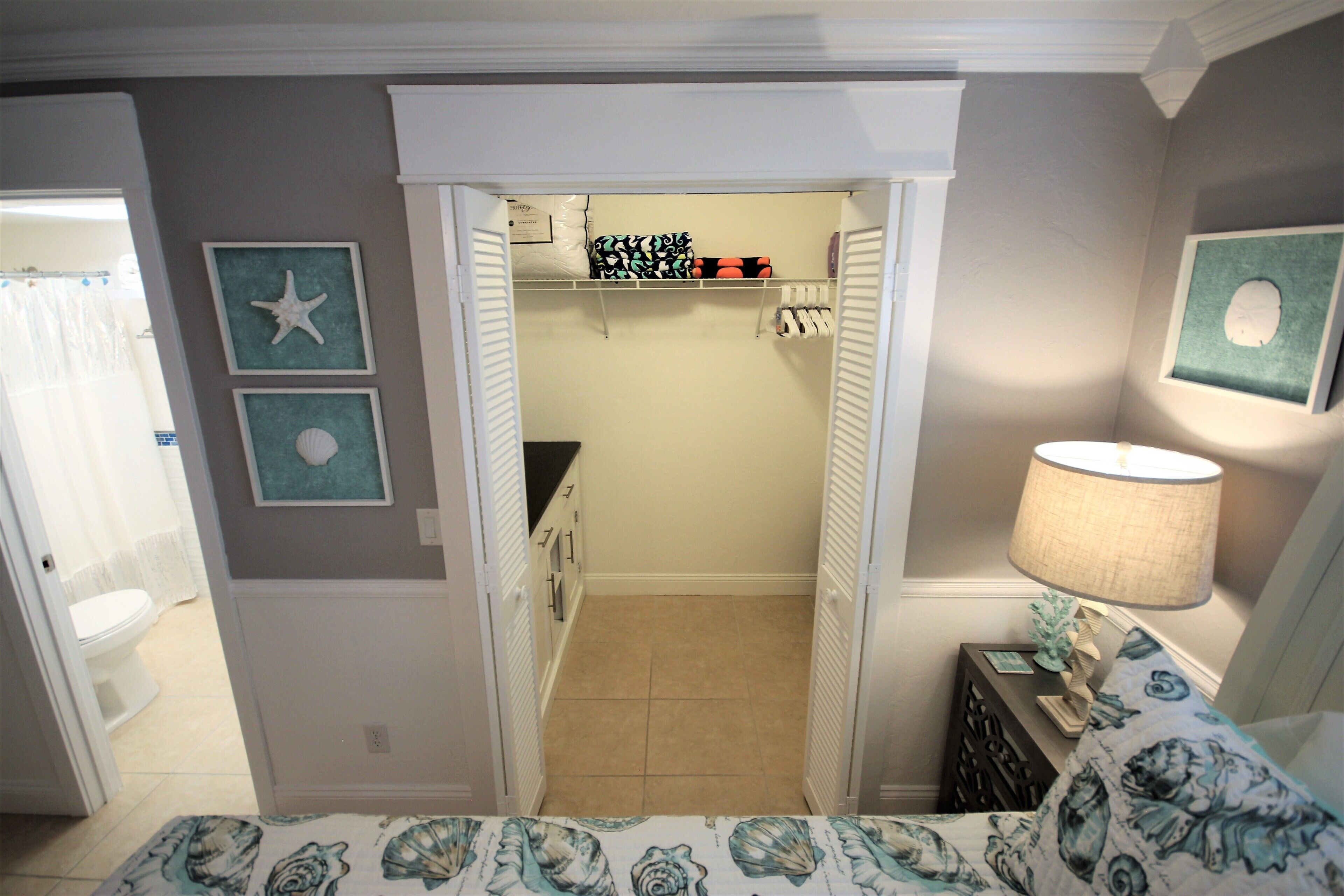 A bedroom with a bed, a nightstand, a lamp, and a closet with shelves and a hanging rack.