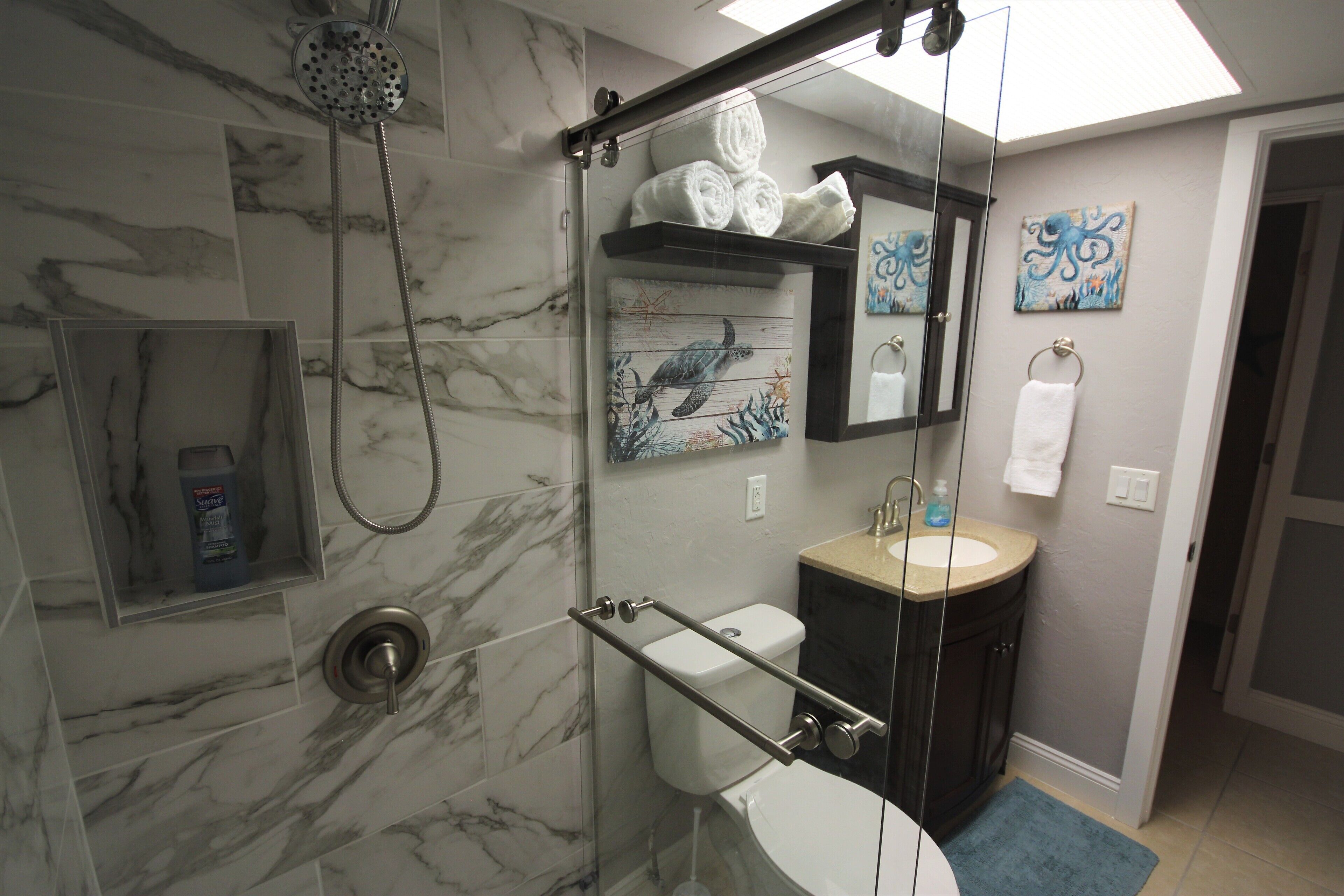 A bathroom with a glass-enclosed shower, a toilet, a sink, and marble walls.