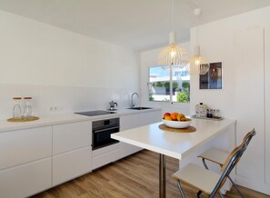 Eine moderne Küche mit weißen Schränken, einem eingebauten Ofen, einer Spüle und einem Fenster mit Blick auf Grünflächen.