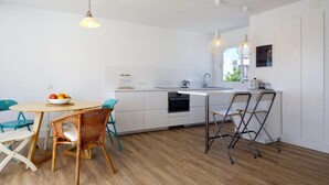 Una cucina moderna con mobili bianchi, un tavolo da pranzo in legno, sedie in vimini e lampade a sospensione.