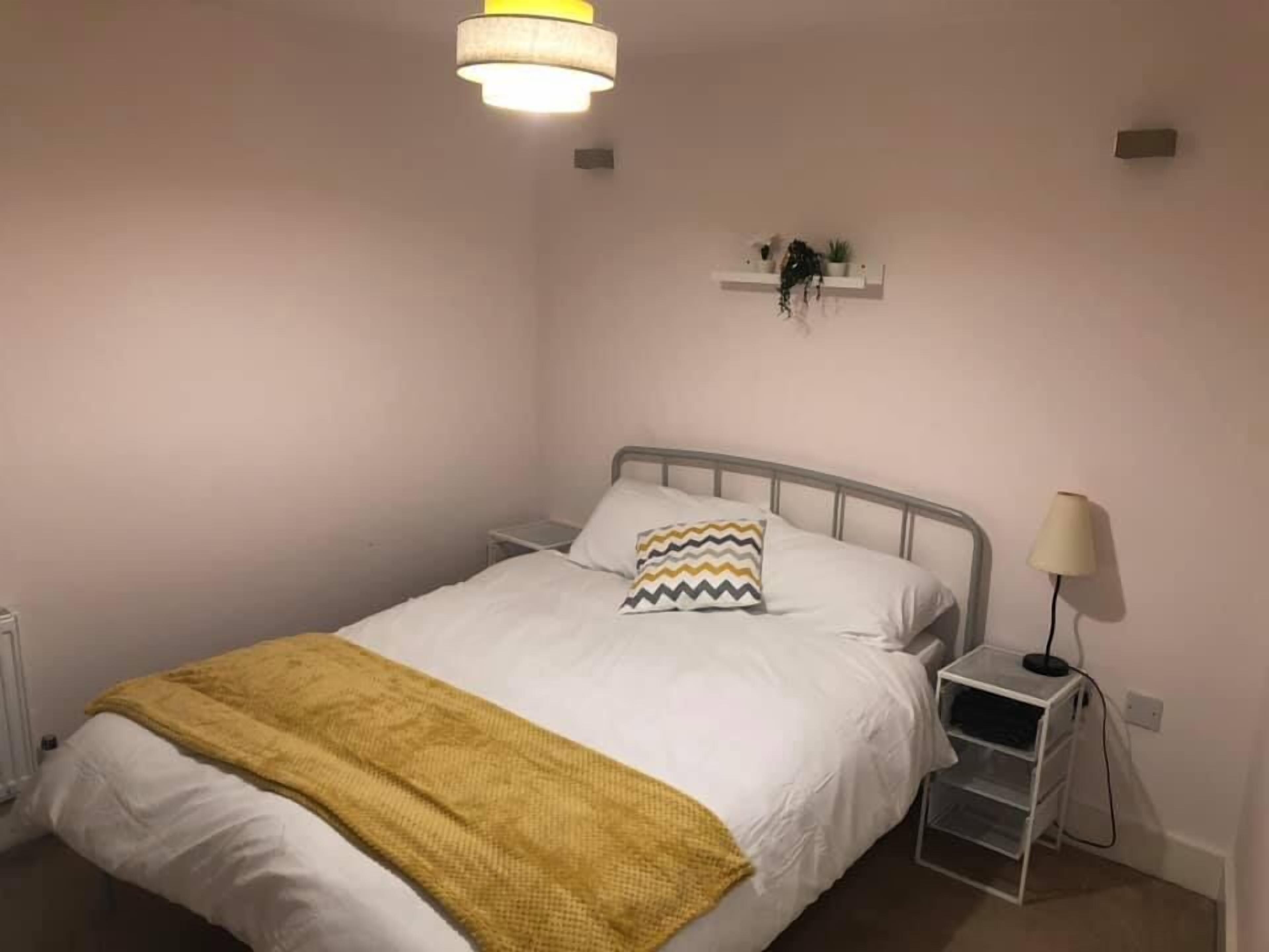 Un dormitorio con cama, mesita de noche, lámpara, estante con plantas y una lámpara colgante.