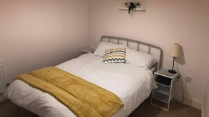 Un dormitorio con cama, mesita de noche, lámpara, estante con plantas y una lámpara colgante.