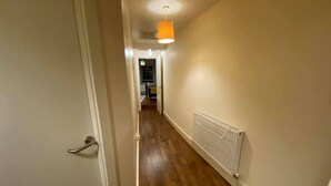 Un pasillo con suelo de madera, un radiador blanco y una lámpara colgante anaranjada.