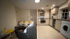 Un espacio habitable compacto con sofá, una mesita, lavadora y kitchenette.