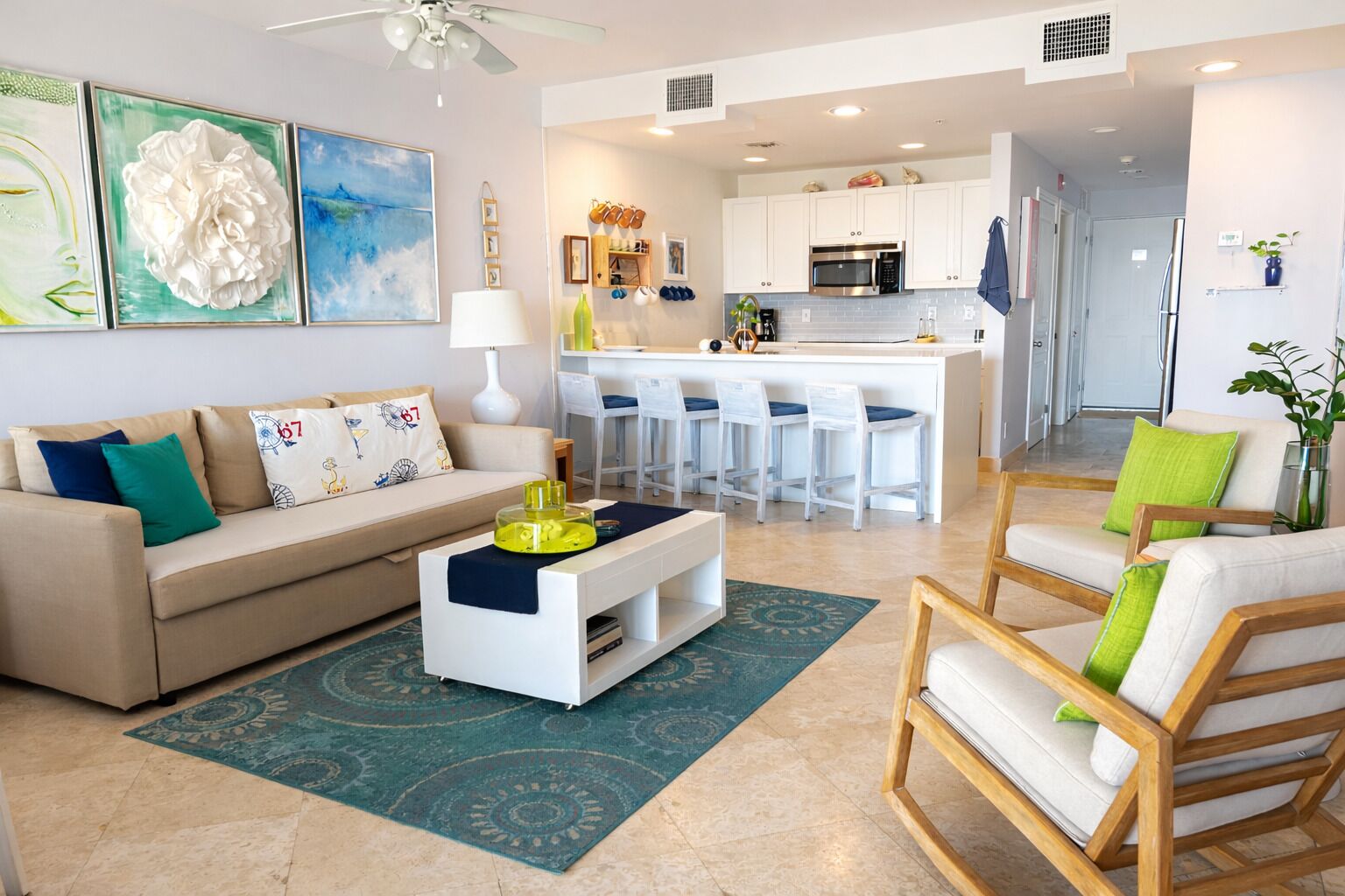 A modern living room with a sofa, coffee table, and chairs, a kitchen with bar stools, and a dining area.