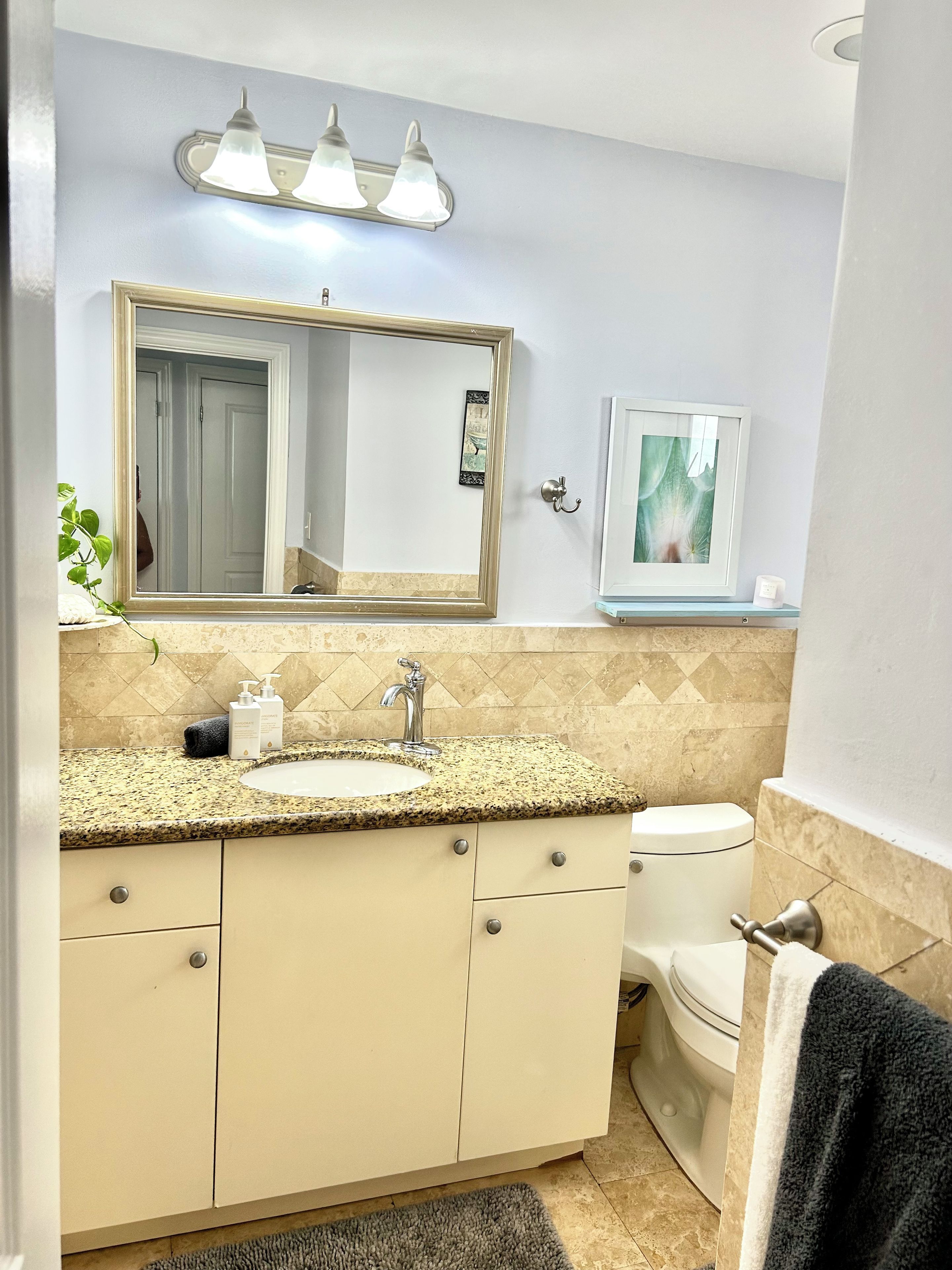 Un baño con lavabo, espejo, tocador, inodoro y perchero para toallas.