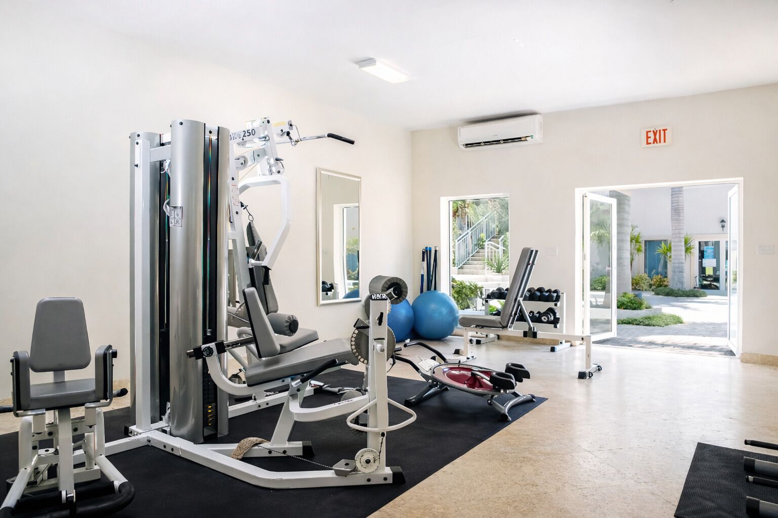 A gym with various exercise machines, a mirror, and a view of the outside.