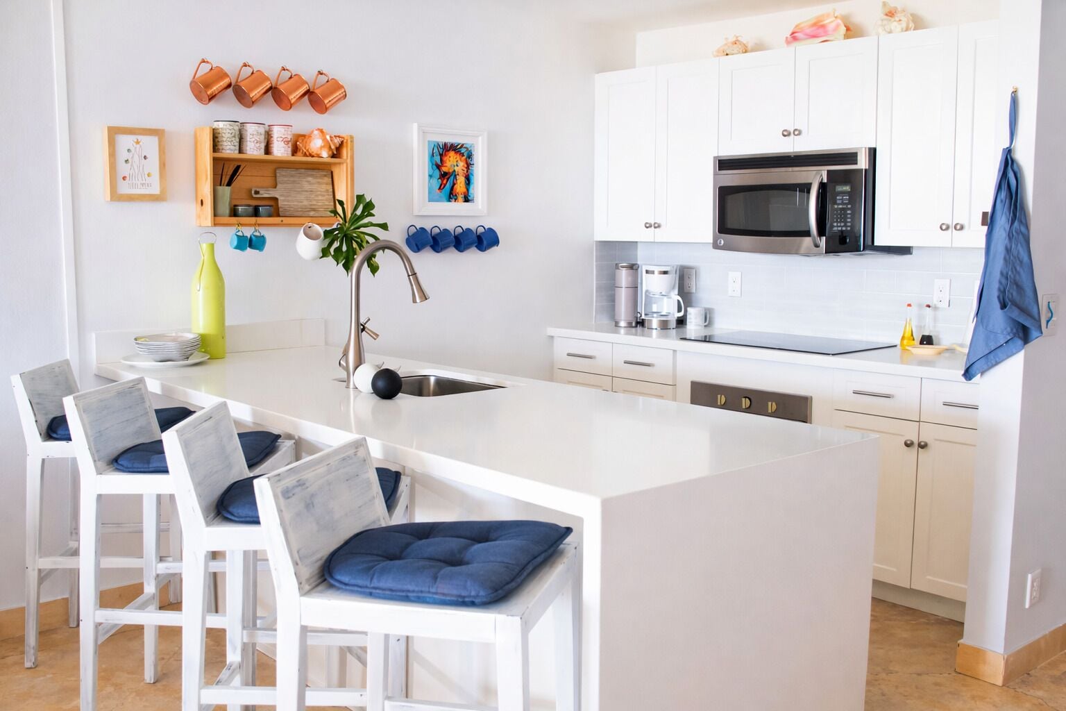 A modern kitchen with white cabinetry, a central island, and a dining area with white chairs and blue cushions.