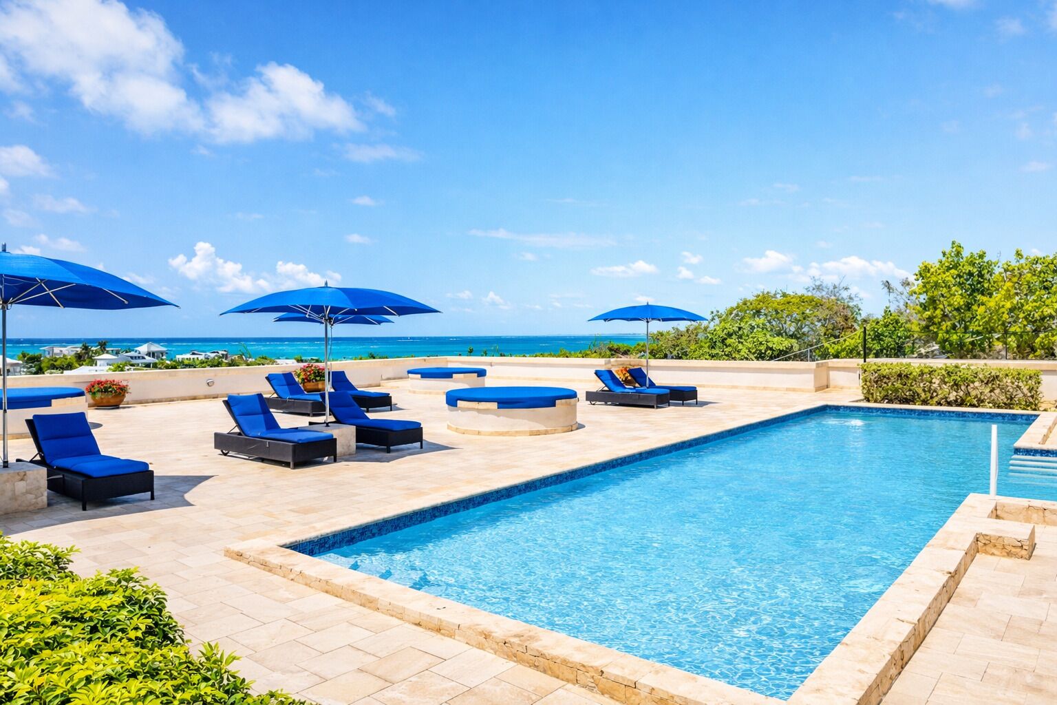 A pool area with lounge chairs and umbrellas, a clear view of the ocean, and a tiled pool edge.