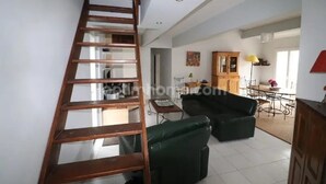 Un escalier menant à une chambre à coucher située en mezzanine, un coin repas avec une table et des chaises, et un salon avec un canapé et une lampe.