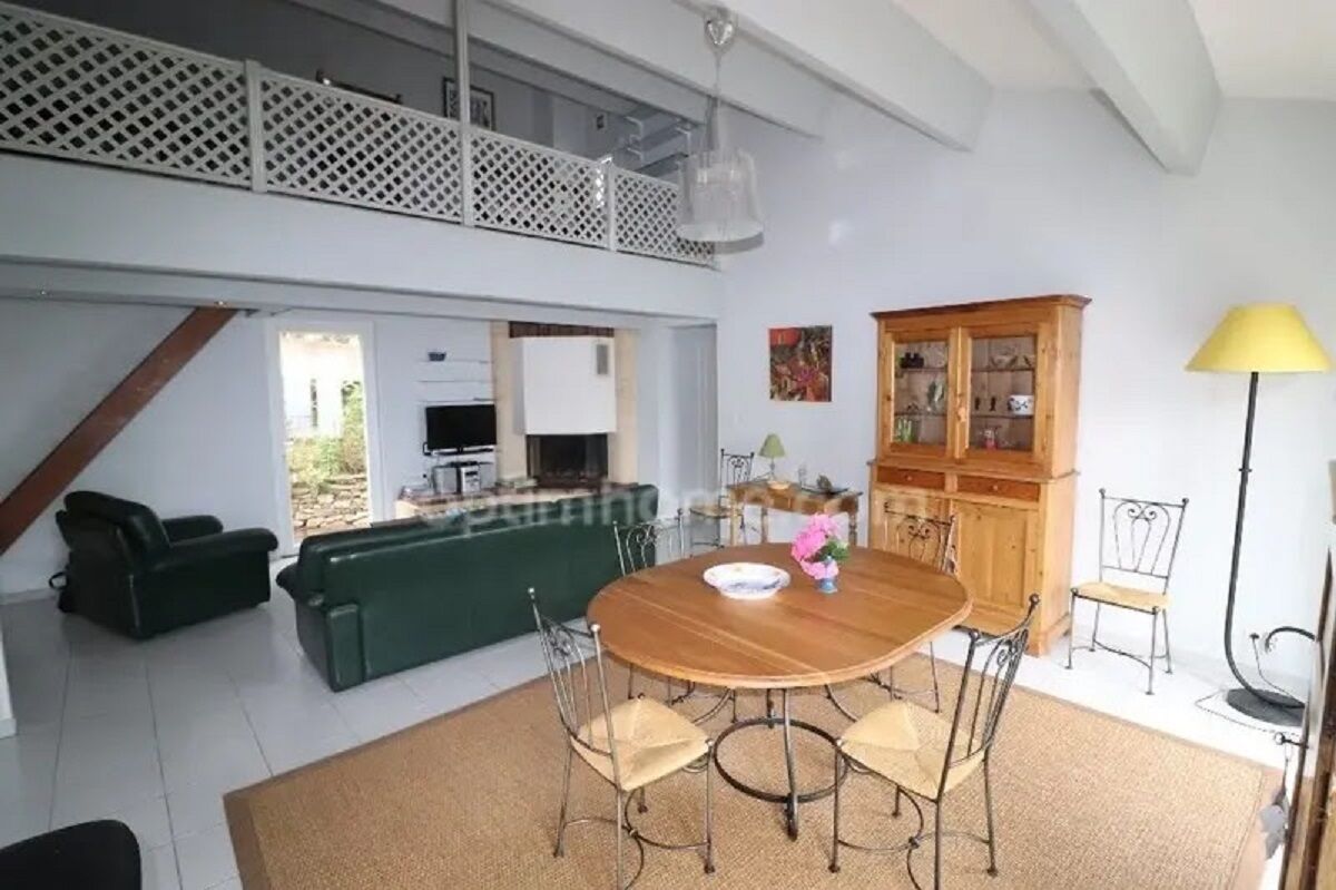 A spacious living area with a dining table, chairs, a sofa, and a high ceiling with a balcony.