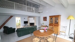 Un vaste espace de vie comprenant une table à manger, des chaises, un canapé et un plafond haut, avec accès à un balcon.