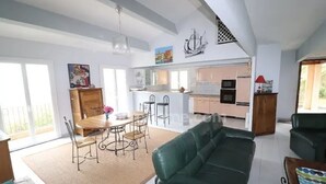 Un vaste salon agrémenté d’un canapé en cuir vert, un coin repas avec une table et des chaises en bois, et une cuisine à l’arrière-plan.
