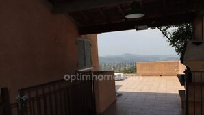 Un espace extérieur abrité, doté d’un sol carrelé, d’un portail en métal et offrant une vue sur les montagnes lointaines.