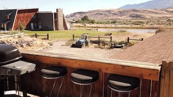 Un coin bar avec trois tabourets, un barbecue et une vue sur un paysage rural avec des montagnes et une étendue d’eau.